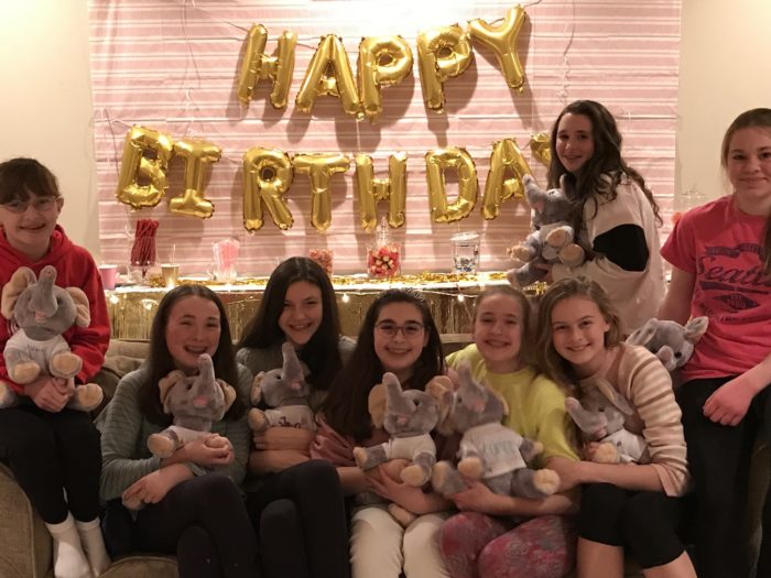 Young girls holding up their fill-a-friend stuffed animals after making them at a party.